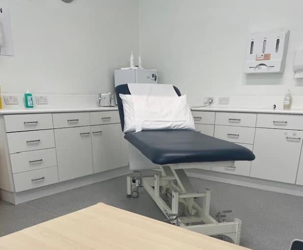 A treatment room at Beechwood House with a navy examination couch and fitted clinical cabinets.