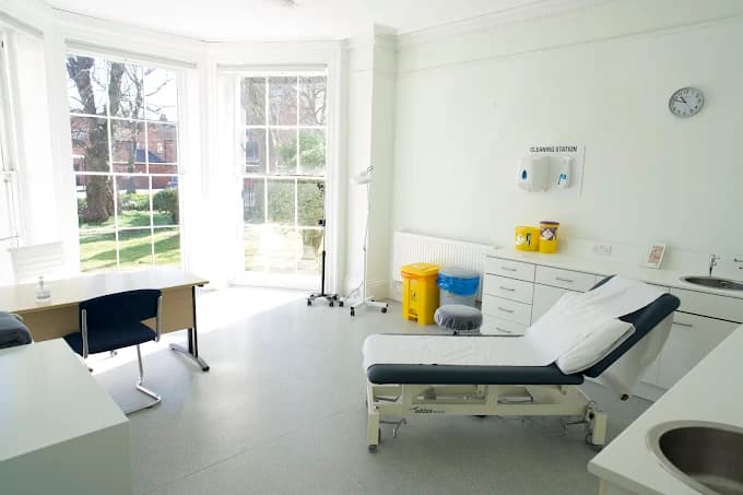 A bright, fully-equipped treatment room at Beechwood House, with an examination couch, clinical sink and a large bay window overlooking the gardens.